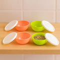 Set of four small round plastic bowls with clear lids for food storage.