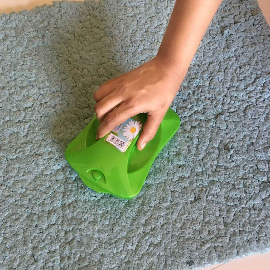 Handheld carpet roller brush efficiently cleaning dust and crumbs from a patterned rug.