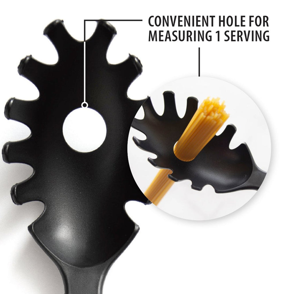 Black heat-resistant pasta server resting on a kitchen counter next to a bowl of pasta.