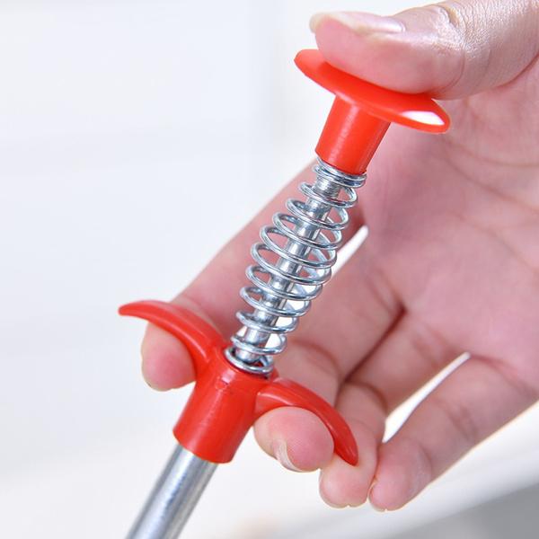 A hand using the drain cleaner to clear a bathroom floor drain.