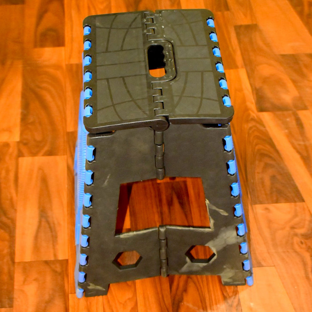 A person standing confidently on the 18-inch plastic step stool to reach a top kitchen cabinet.