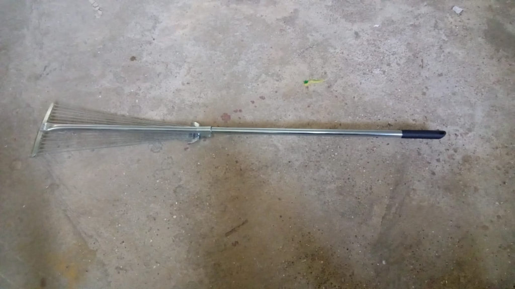 A gardener using the versatile garden rake to smooth soil in a neatly maintained yard.