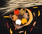 A round plastic masala spice box with seven compartments and a clear lid, showcasing vibrant spices.