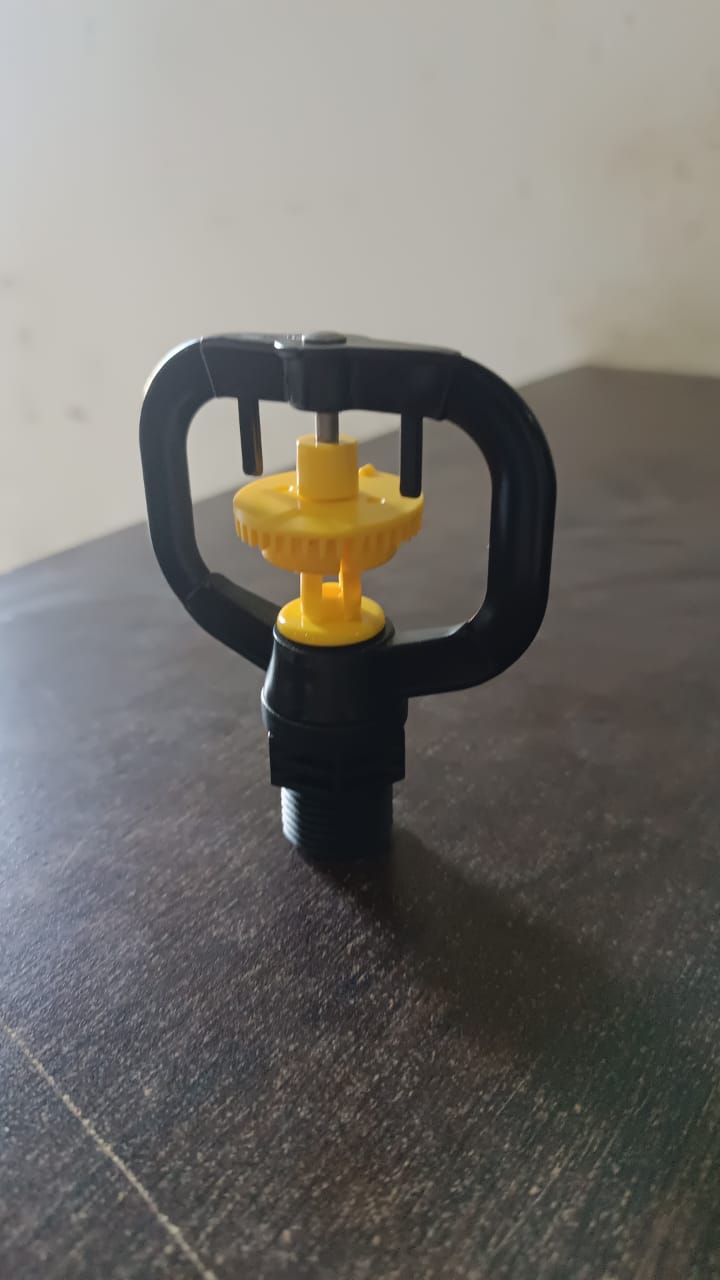 Rotating irrigation sprinkler nozzle actively spraying water in a garden bed.
