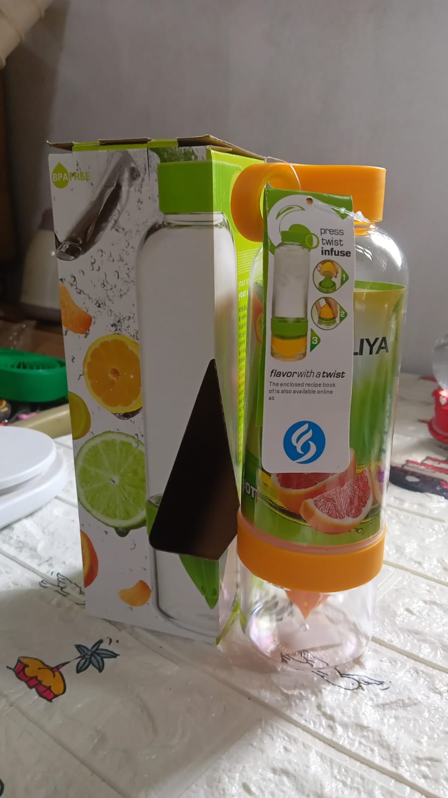 Lifestyle shot of the fruit infuser sports bottle surrounded by fresh citrus fruits and water.