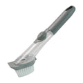 Soap-dispensing dish brush actively scrubbing a greasy pan in a kitchen