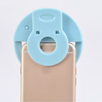 LED selfie ring light held by hand, shining bright light on a smartphone.