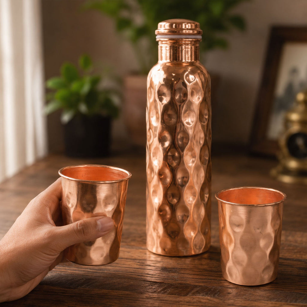 Diamond cut copper water bottle set with two matching glasses on a light background.