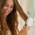 Hand pressing the quick-release button on the Self-Cleaning Hair Brush to remove trapped hair.