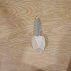A white plastic measuring spoon demonstrating its use as a bag clip on a food bag.