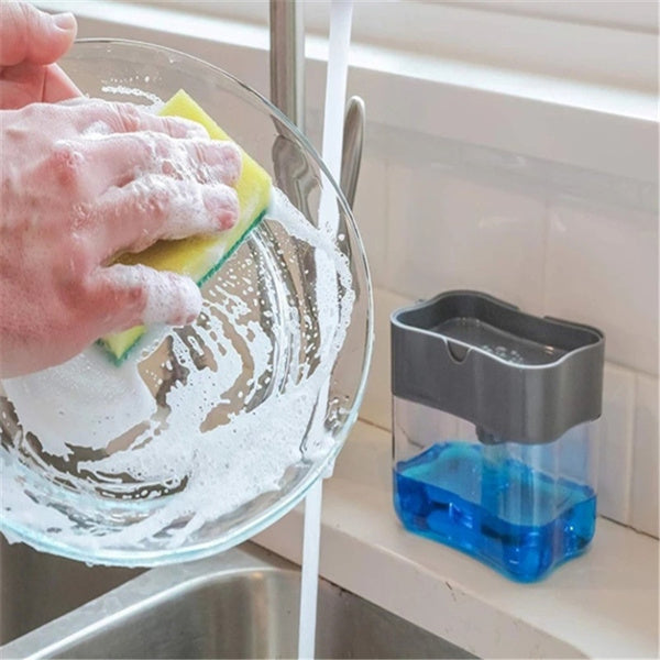 A grey 2-in-1 soap dispenser with a clean white sponge on a kitchen countertop.