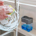 A grey 2-in-1 soap dispenser with a clean white sponge on a kitchen countertop.