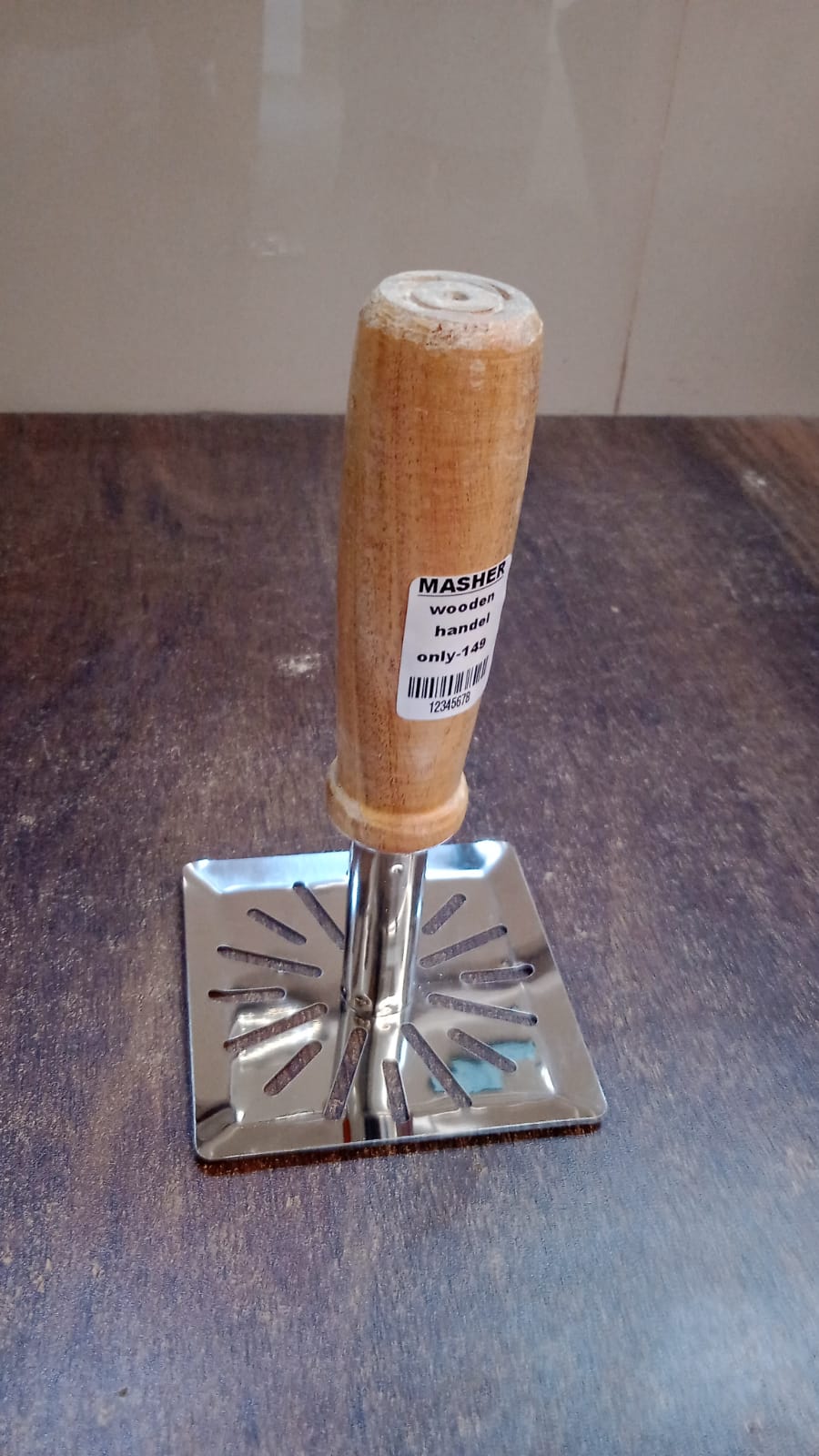 Stainless steel potato masher with wooden handle hanging on kitchen rack