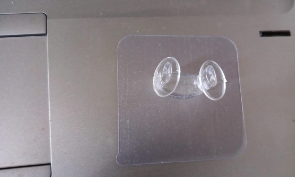 Minimalist transparent self-adhesive wall hook installed on a white wall.