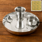 Stainless steel pooja thali set with katori, glass, and spoon on a white background.