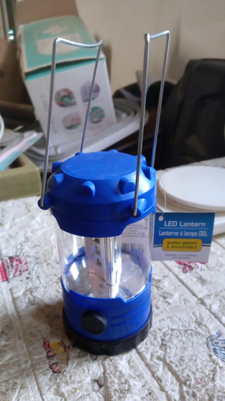 Camping lantern glowing brightly in an outdoor setting at dusk.