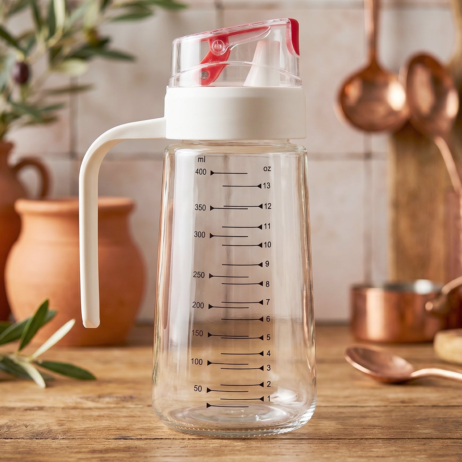 Glass oil dispenser bottle with auto-flip cap, side handle, and measurement scale for precise kitchen pouring