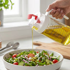 Olive oil being drizzled from glass dispenser onto a fresh salad