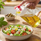 Hand pouring olive oil from glass dispenser with auto-flip lid onto salad
