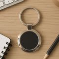 Round metal keychain with black center and chrome finish on white background.