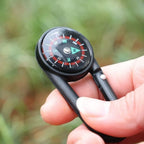 Mini compass with clip attached to a backpack strap, showing its compact size for outdoor use.