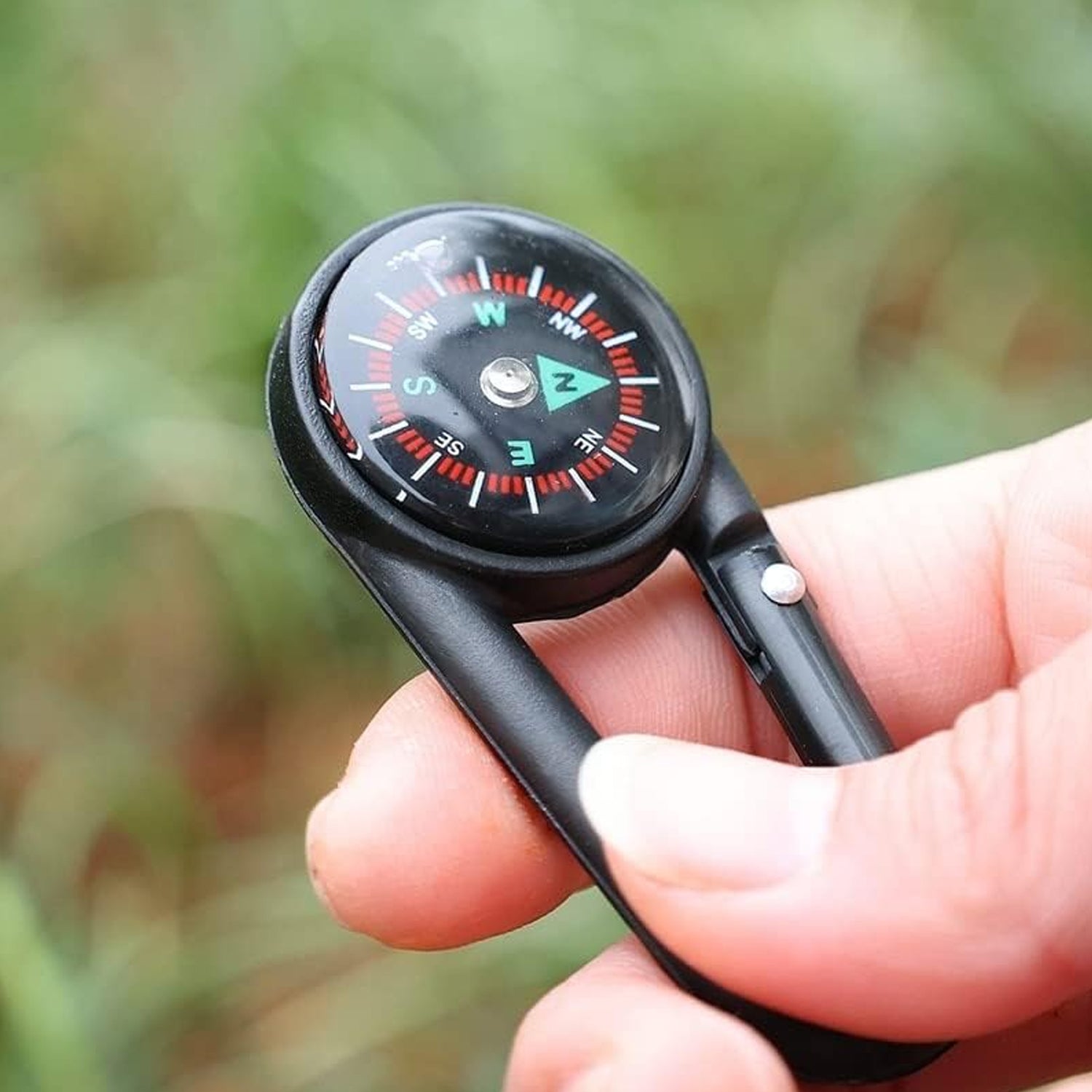 Mini compass with clip attached to a backpack strap, showing its compact size for outdoor use.
